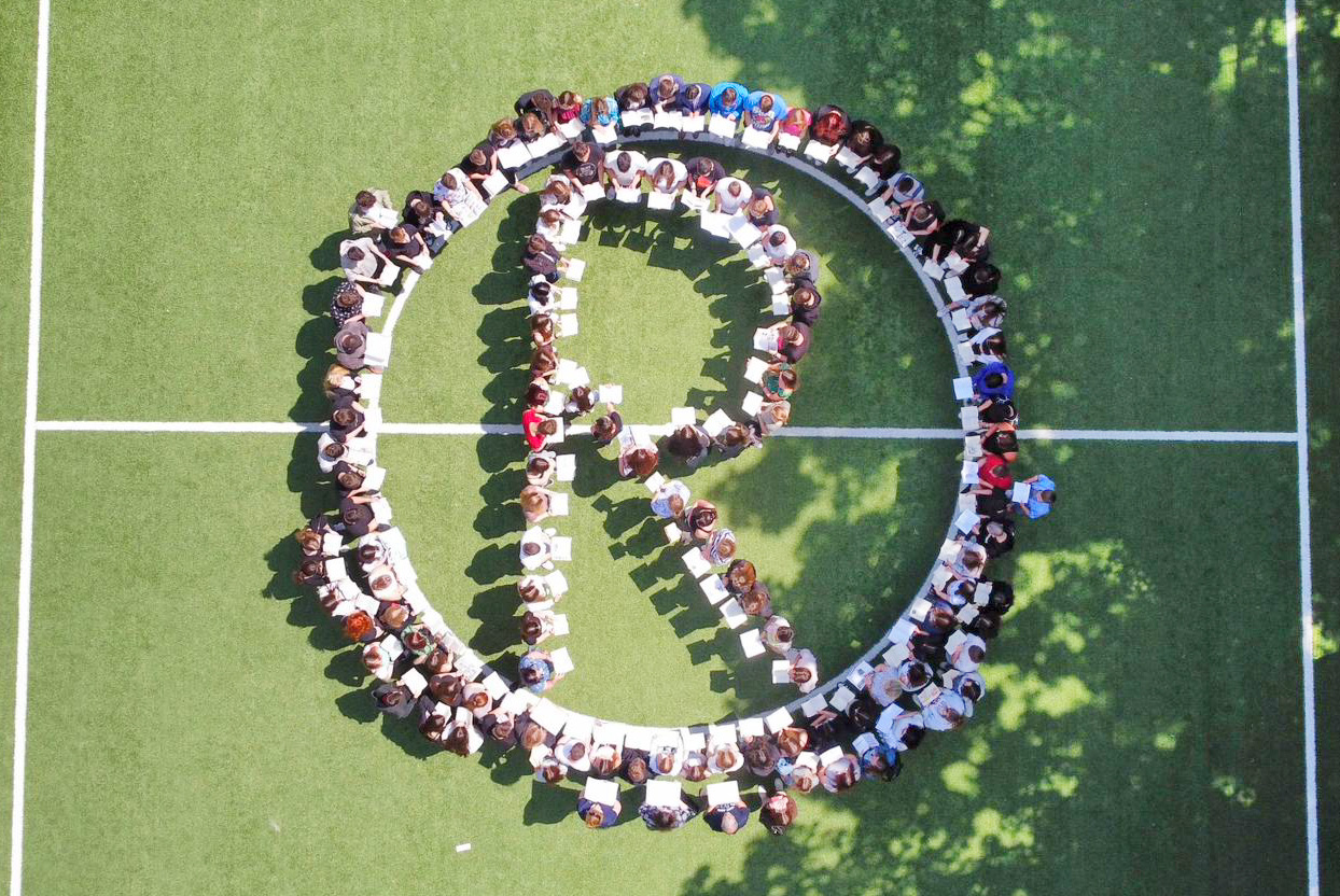 Zdjęcie z drona z lotu ptaka przedstawia kilkudziesięciu uczniów tworzących literę R na boisku szkolnym