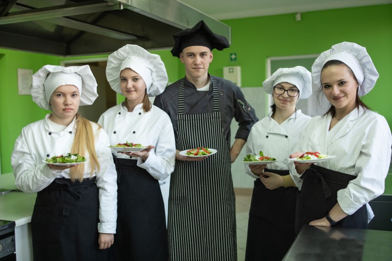 Uczniowie w kuchni, każdy trzyma w dłoni talerz z przygotowaną potrawą.